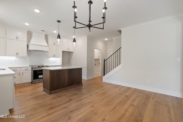 kitchen with custom range hood, white cabinets, light hardwood / wood-style floors, and stainless steel stove