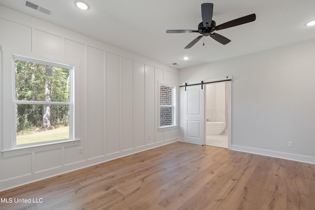 unfurnished bedroom featuring connected bathroom, ceiling fan, light wood-type flooring, and a barn door