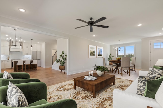 living room with ornamental molding, ceiling fan with notable chandelier, and light wood-type flooring