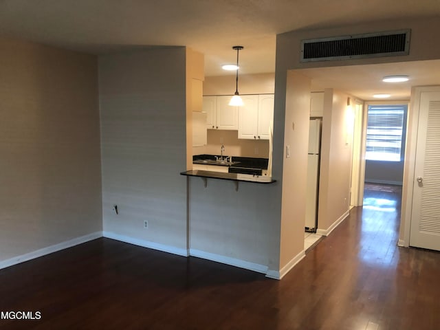 kitchen featuring dark hardwood / wood-style flooring, kitchen peninsula, white cabinetry, pendant lighting, and white refrigerator