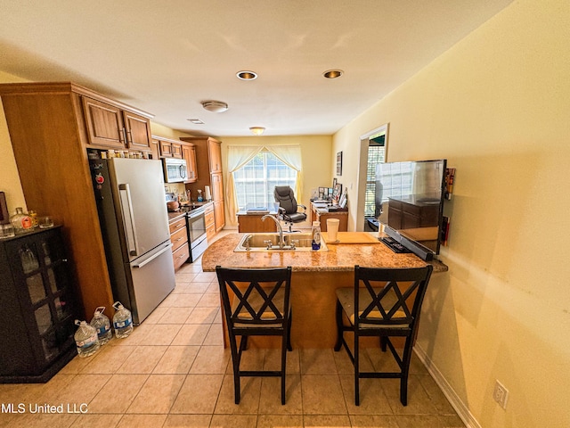 kitchen featuring kitchen peninsula, a breakfast bar area, light tile patterned flooring, sink, and stainless steel appliances