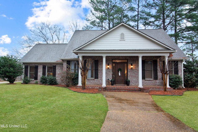 view of front of property with a shingled roof, a front yard, covered porch, and brick siding