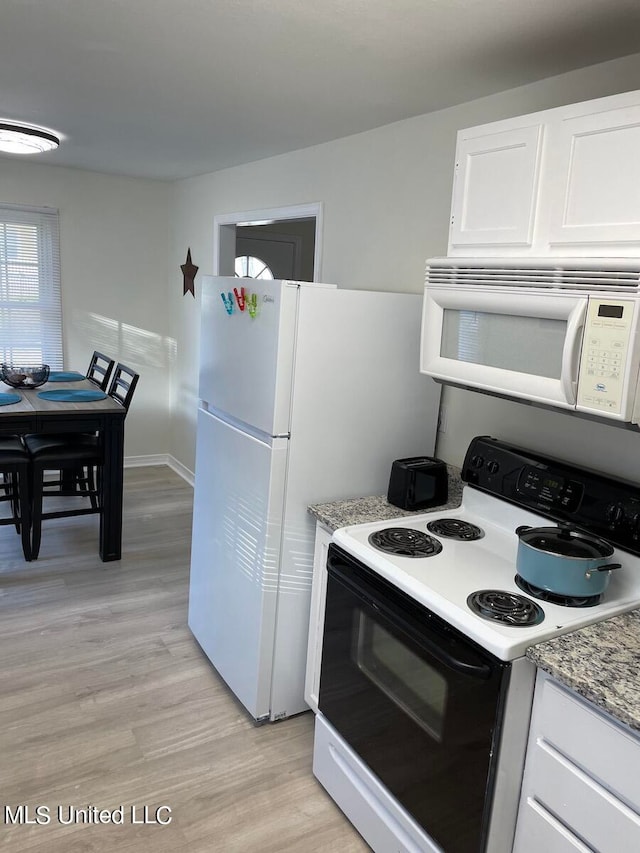 kitchen with white appliances, light stone counters, light wood-type flooring, and white cabinets