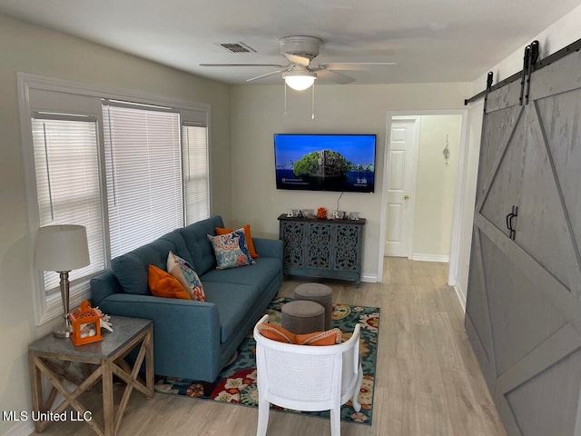 living room with a barn door, light wood-type flooring, and ceiling fan