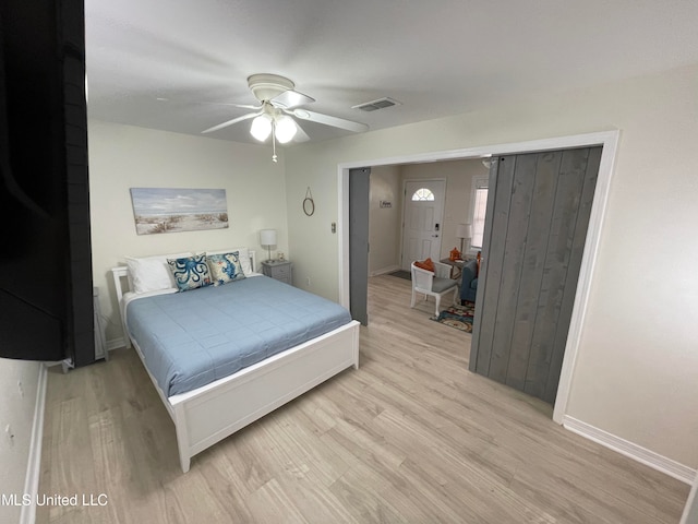 bedroom with a barn door, light hardwood / wood-style floors, and ceiling fan