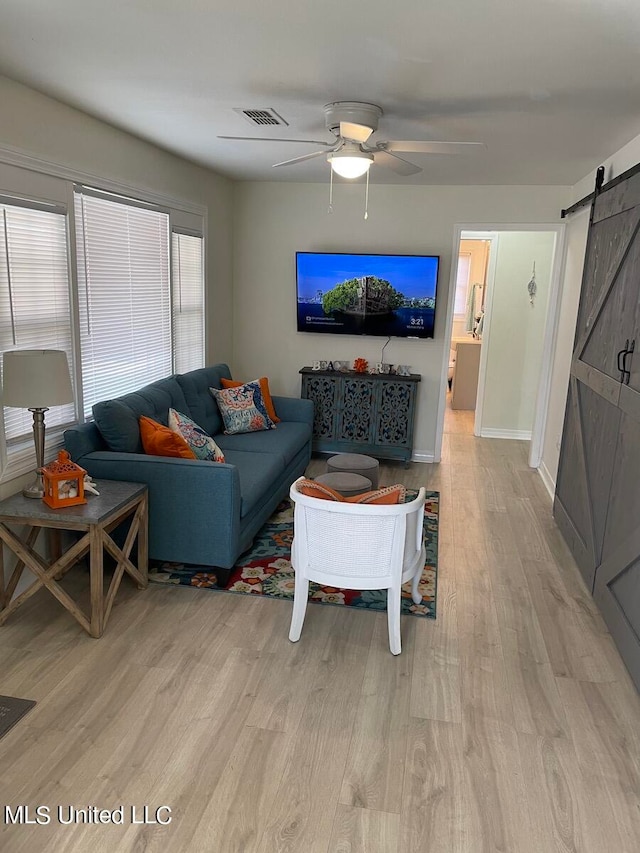 living room featuring ceiling fan, light wood-type flooring, and a barn door