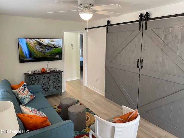 living room with a barn door, light wood-type flooring, and ceiling fan