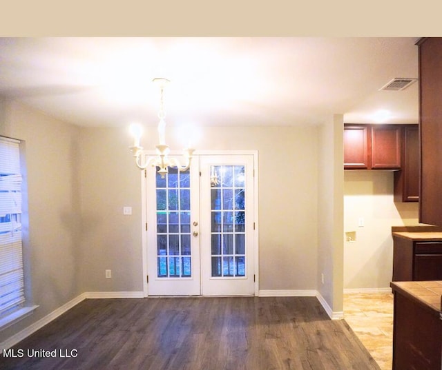 unfurnished dining area featuring visible vents, an inviting chandelier, baseboards, and wood finished floors