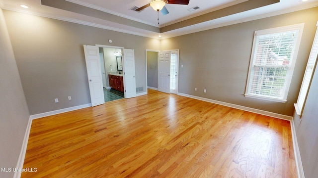 unfurnished bedroom featuring a tray ceiling, ornamental molding, baseboards, light wood-style floors, and connected bathroom