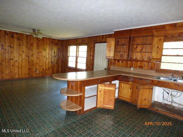 kitchen featuring ceiling fan, a sink, a textured ceiling, wood walls, and brown cabinetry