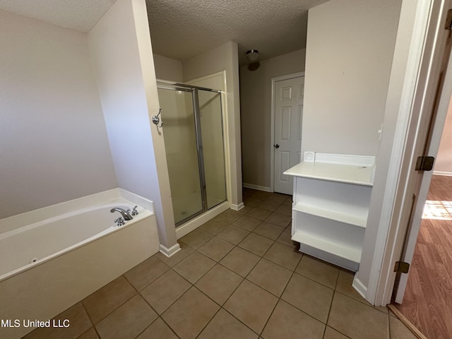 bathroom with a garden tub, a stall shower, a textured ceiling, tile patterned flooring, and baseboards