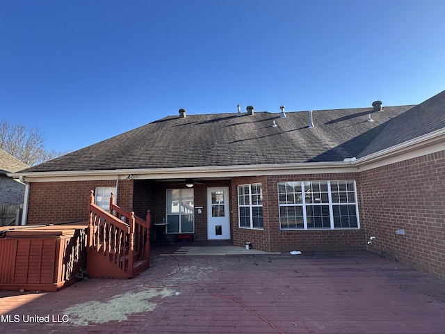 back of property featuring a deck, brick siding, a shingled roof, and a hot tub