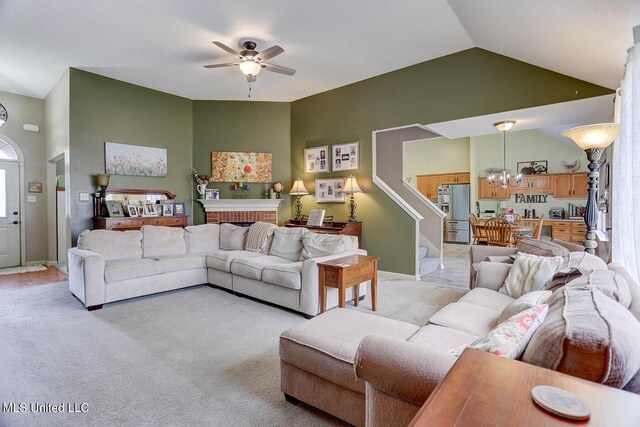 living area with light carpet, lofted ceiling, stairs, and ceiling fan with notable chandelier