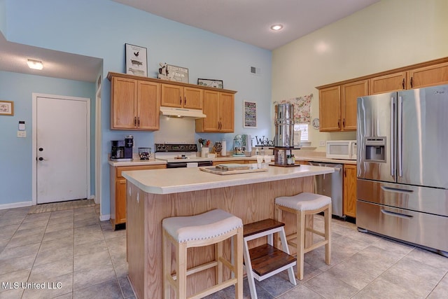 kitchen with stainless steel appliances, a towering ceiling, a kitchen bar, light countertops, and under cabinet range hood