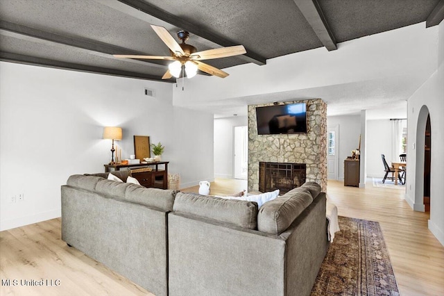 living room with light wood-type flooring, a fireplace, a textured ceiling, ceiling fan, and beam ceiling