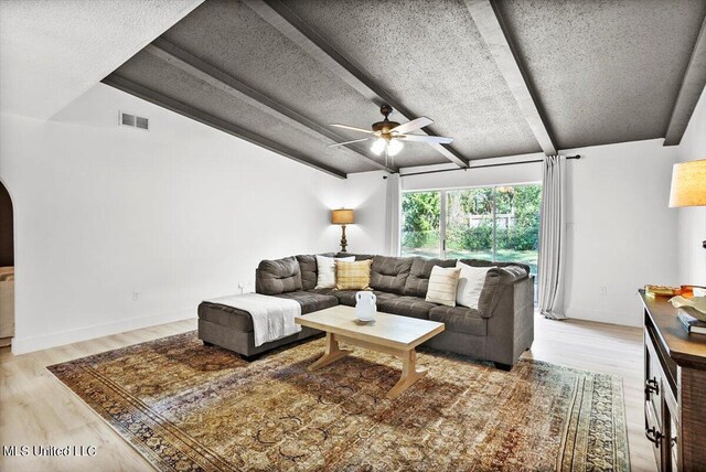 living room featuring lofted ceiling with beams, light hardwood / wood-style flooring, a textured ceiling, and ceiling fan