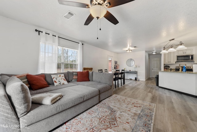 living room with ceiling fan, light hardwood / wood-style floors, and a textured ceiling