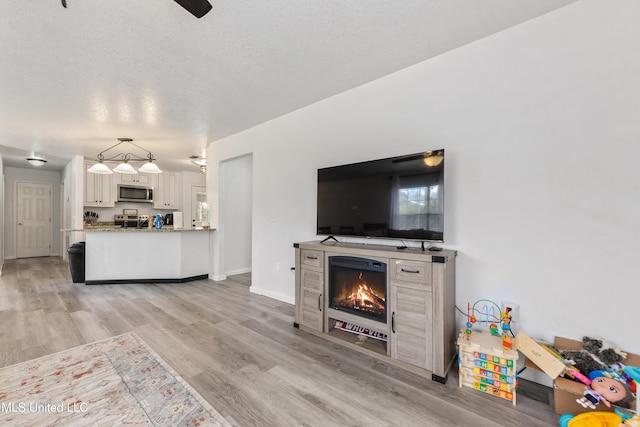 living room featuring ceiling fan, light hardwood / wood-style floors, and a textured ceiling