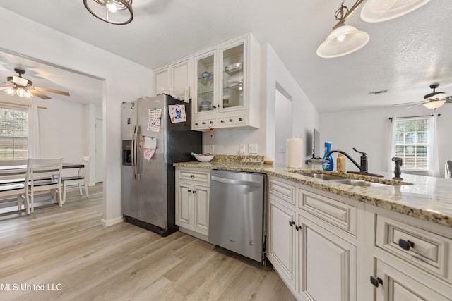 kitchen with sink, hanging light fixtures, light stone counters, light hardwood / wood-style floors, and stainless steel appliances