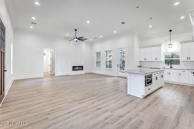 kitchen with white cabinetry, a center island, ceiling fan, a large fireplace, and hanging light fixtures