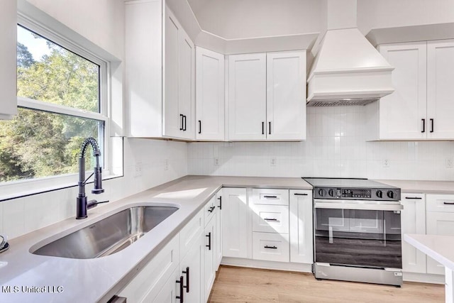 kitchen with sink, range with electric cooktop, white cabinets, and custom range hood