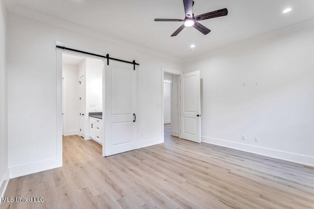 unfurnished bedroom featuring ceiling fan, ensuite bath, a barn door, and crown molding