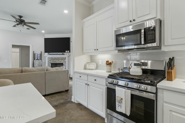 kitchen featuring appliances with stainless steel finishes, decorative backsplash, a fireplace, white cabinets, and ornamental molding