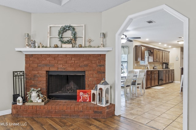 living room featuring ceiling fan, a textured ceiling, a brick fireplace, and light wood-type flooring