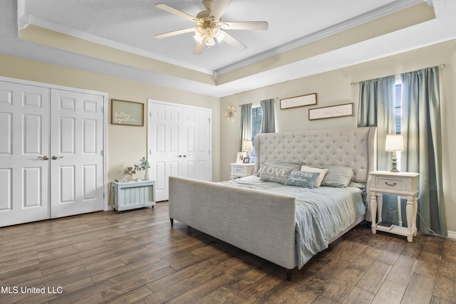 bedroom featuring a raised ceiling, ornamental molding, dark wood-type flooring, and multiple closets