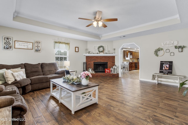 living room with a raised ceiling, crown molding, a fireplace, and dark hardwood / wood-style flooring