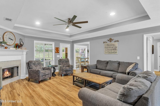 living room with light hardwood / wood-style floors, a raised ceiling, ornamental molding, and a tile fireplace