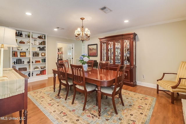 dining area with light hardwood / wood-style floors, ornamental molding, and a chandelier