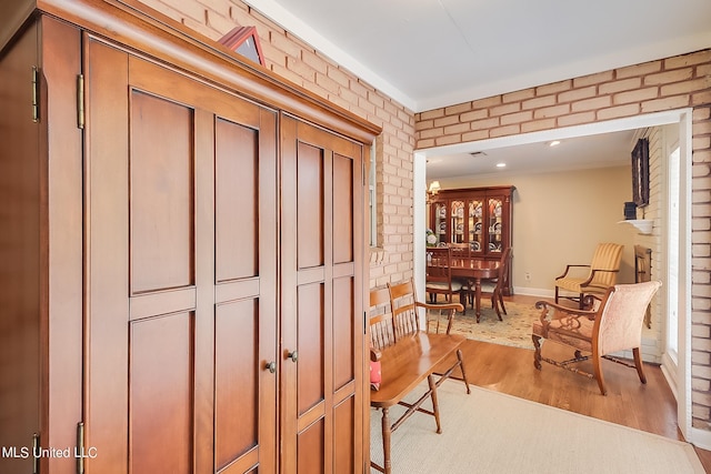 hall with brick wall, light hardwood / wood-style flooring, and an inviting chandelier