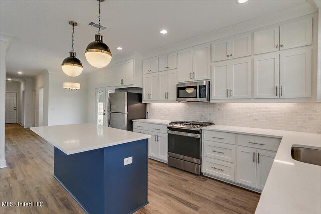 kitchen featuring appliances with stainless steel finishes, pendant lighting, white cabinetry, and light hardwood / wood-style floors