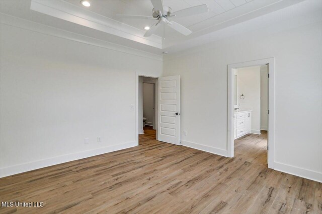 unfurnished bedroom featuring light hardwood / wood-style flooring, ensuite bath, a tray ceiling, and ceiling fan