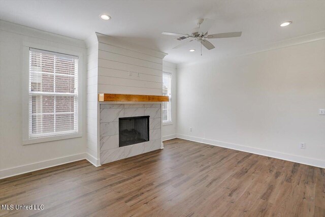 unfurnished living room featuring ceiling fan, a wealth of natural light, a high end fireplace, and dark hardwood / wood-style flooring