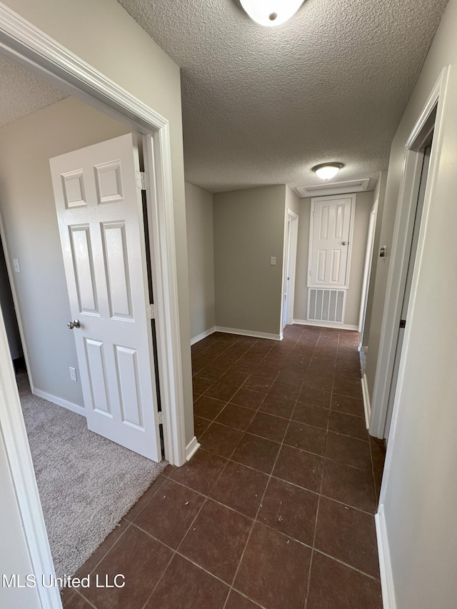 hall with dark tile patterned floors and a textured ceiling