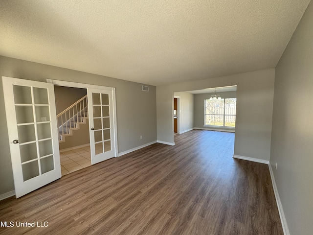 empty room featuring a notable chandelier, wood-type flooring, french doors, and a textured ceiling