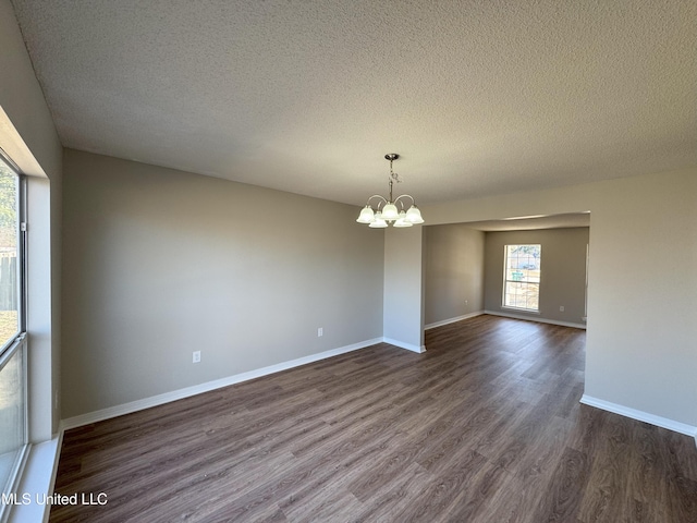 empty room featuring a textured ceiling, a notable chandelier, and dark hardwood / wood-style flooring