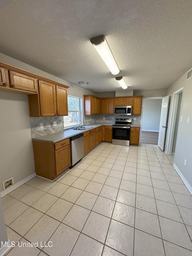 kitchen featuring tasteful backsplash, sink, light tile patterned floors, stainless steel appliances, and a textured ceiling