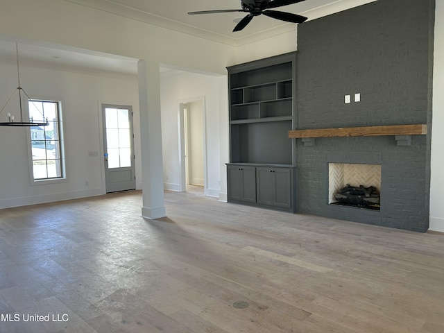 unfurnished living room featuring crown molding, built in features, light hardwood / wood-style flooring, and a brick fireplace