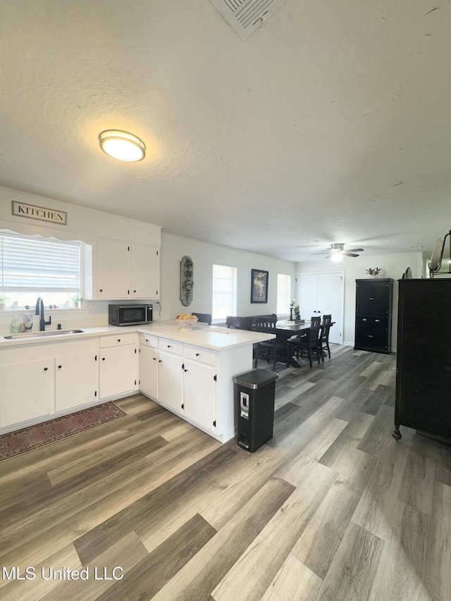 kitchen with sink, light hardwood / wood-style floors, a textured ceiling, white cabinets, and kitchen peninsula