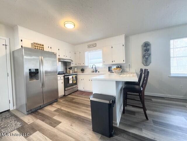 kitchen with white cabinetry, stainless steel appliances, a textured ceiling, a kitchen bar, and kitchen peninsula