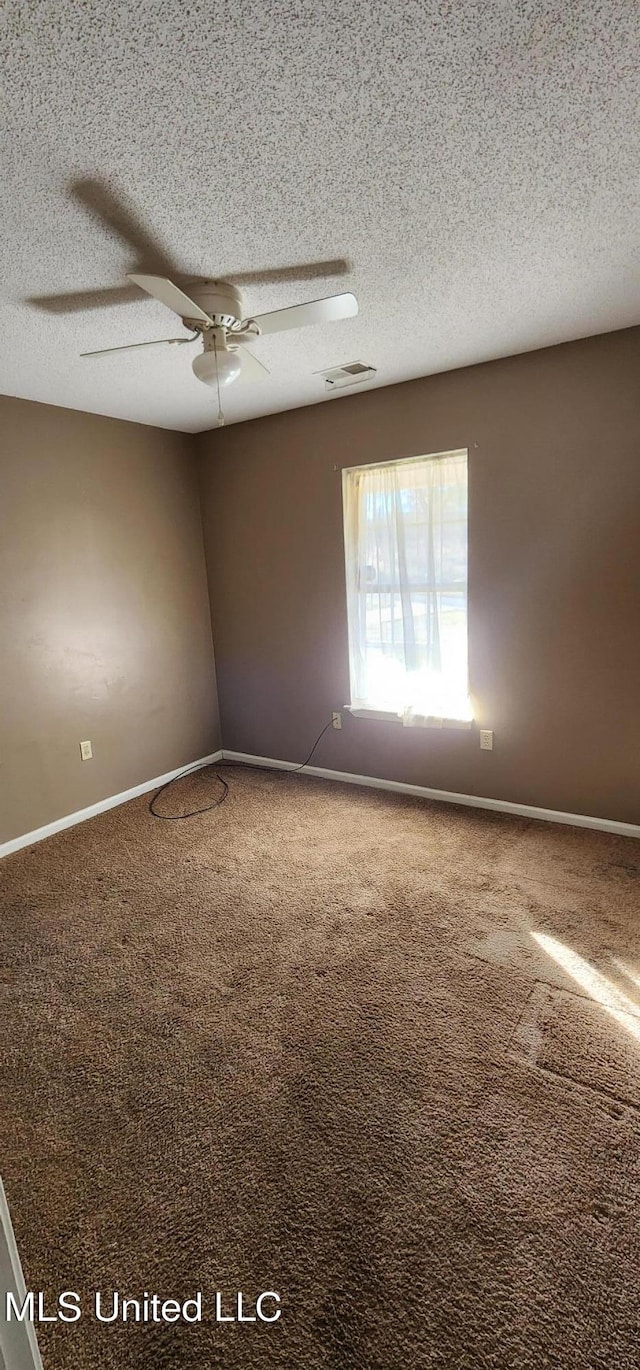 carpeted empty room featuring a textured ceiling, ceiling fan, baseboards, and visible vents