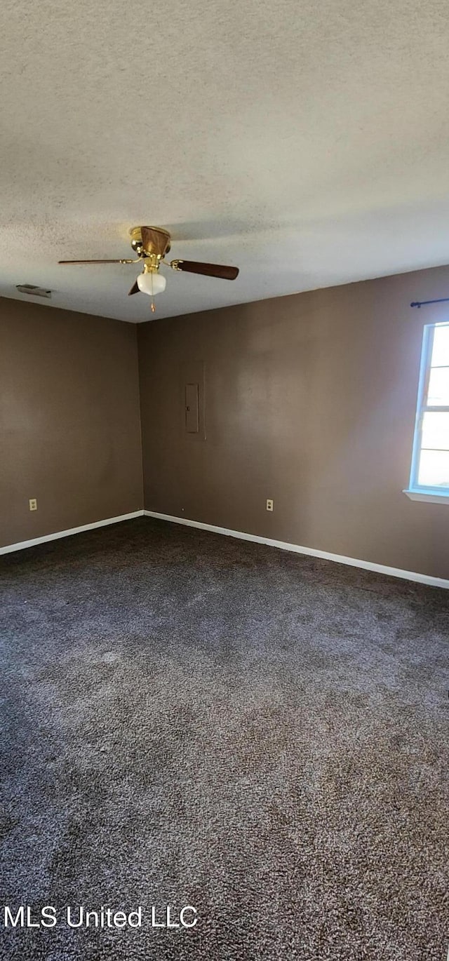 empty room with dark carpet, baseboards, ceiling fan, and a textured ceiling