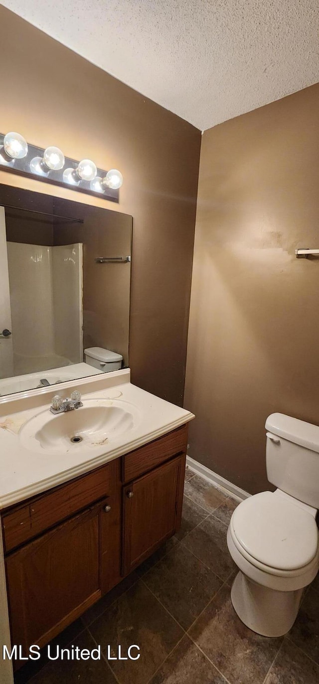 bathroom featuring a textured ceiling, vanity, tile patterned flooring, toilet, and baseboards