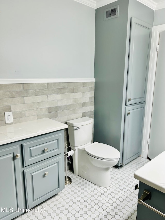 bathroom featuring vanity, ornamental molding, toilet, and tile walls