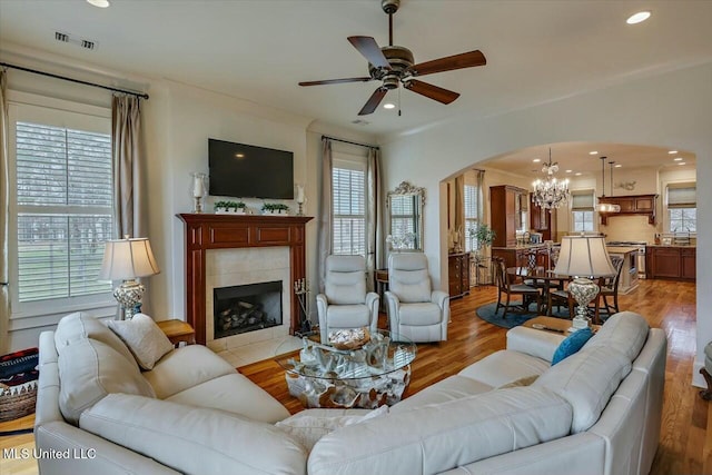 living room with a tiled fireplace, ceiling fan with notable chandelier, and light wood-type flooring