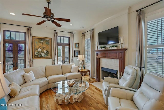 living room featuring a tiled fireplace, light hardwood / wood-style flooring, french doors, and ceiling fan