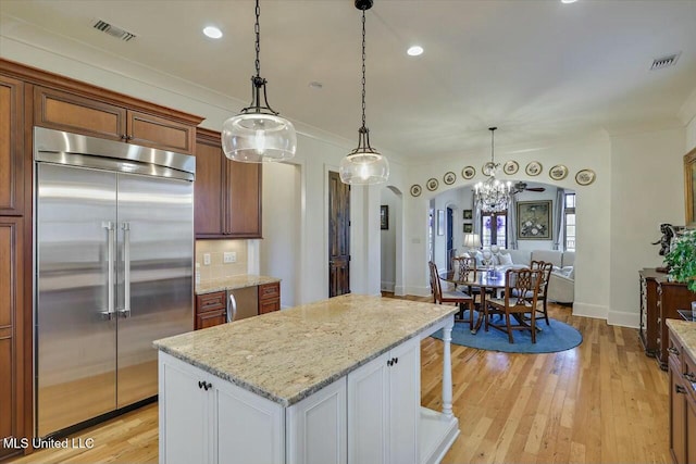 kitchen with crown molding, stainless steel built in fridge, pendant lighting, light stone countertops, and white cabinets